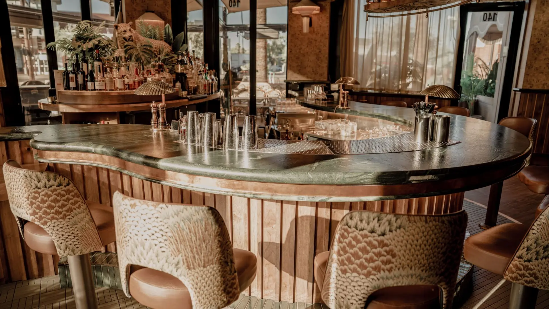 Curved restaurant bar with a polished green stone top, rounded edge and fluted wood front, lined with patterned bar stools