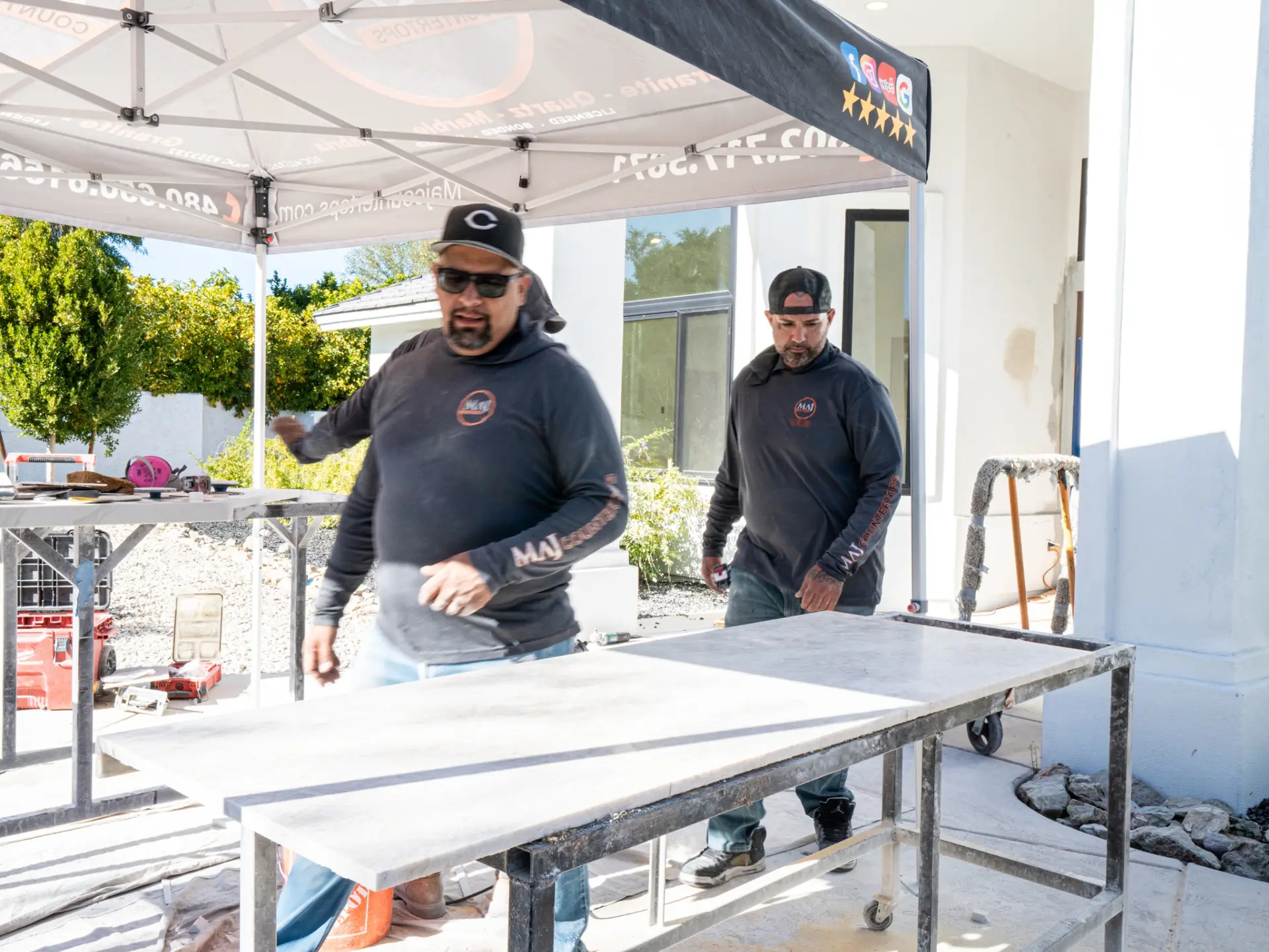 Two MAJ Countertops crew members checking a white stone slab on a work table under a tent