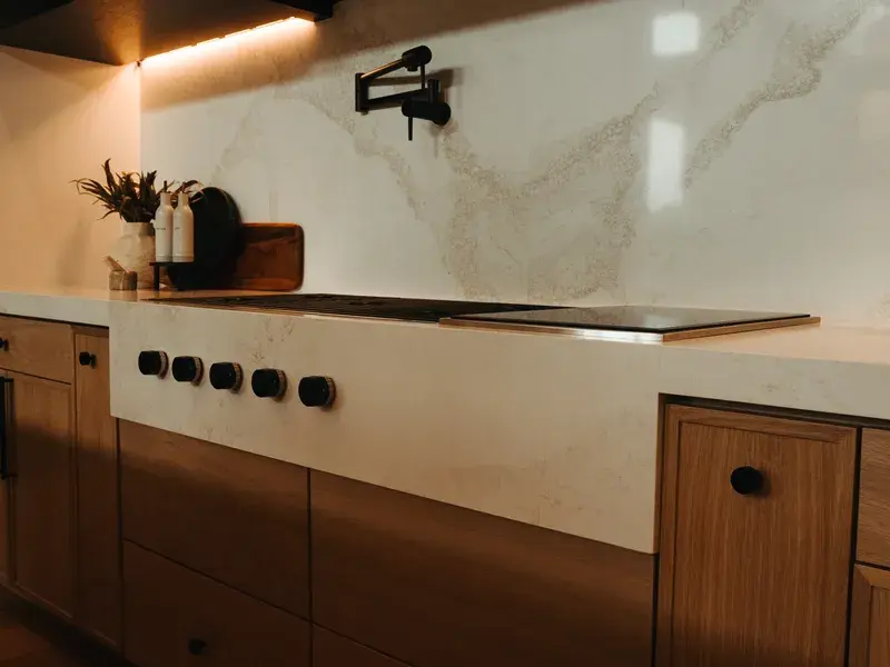Quartz waterfall cooktop counter with a full-height stone backsplash and wood cabinets
