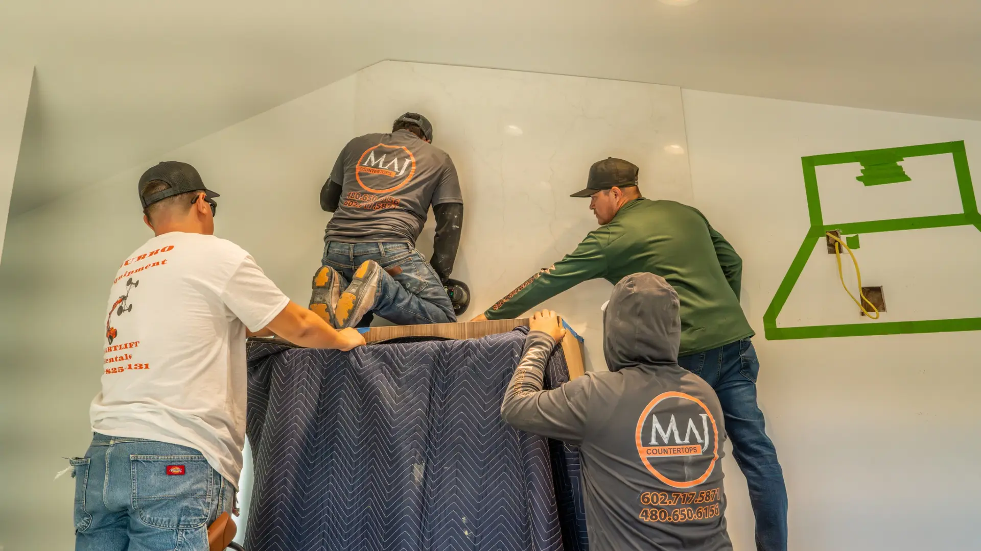 Four MAJ Countertops installers lifting a wrapped stone slab into place