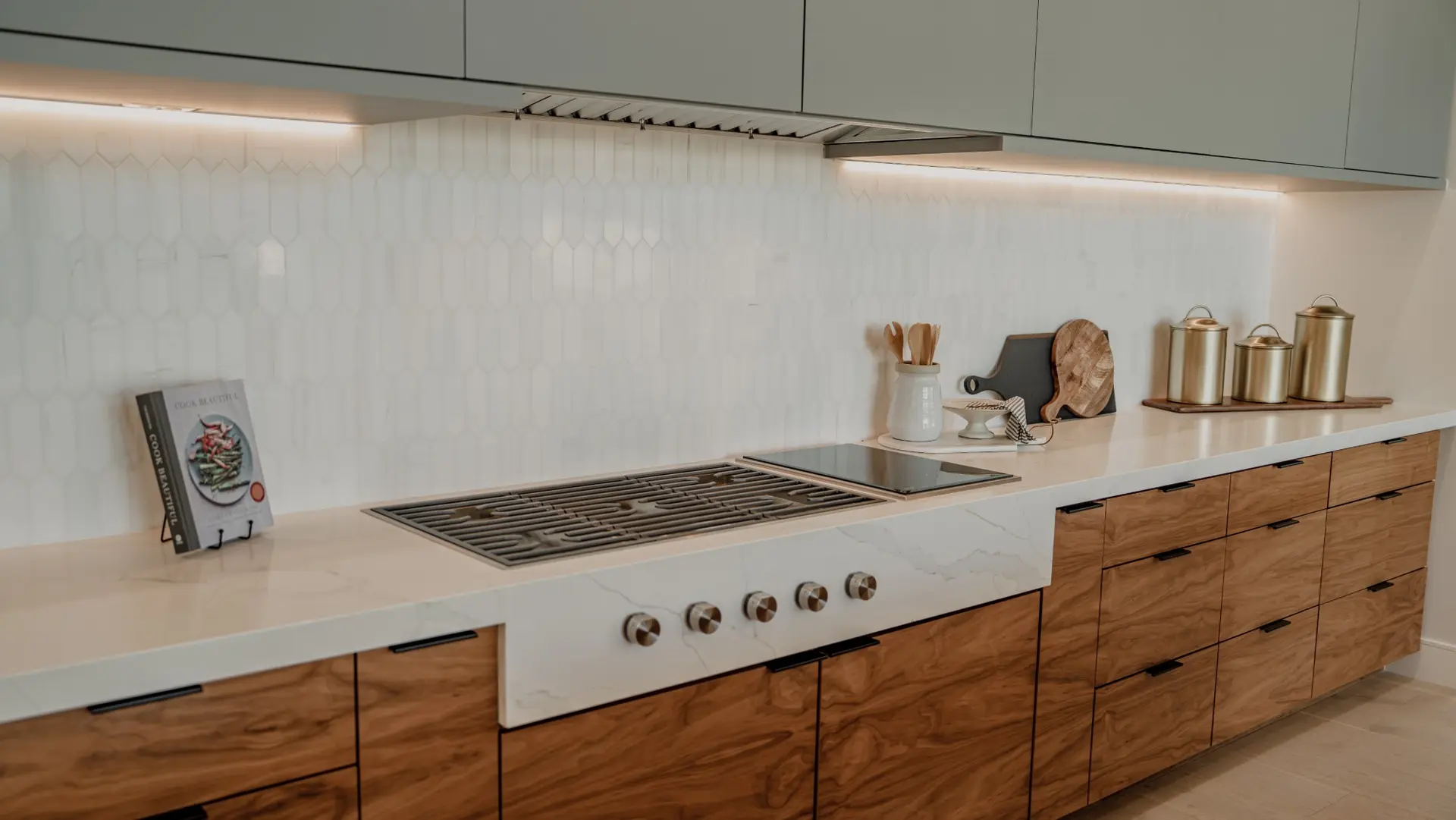 White veined stone countertop that steps down at the cooktop, with the stone running down the front around the control knobs, over walnut cabinets
