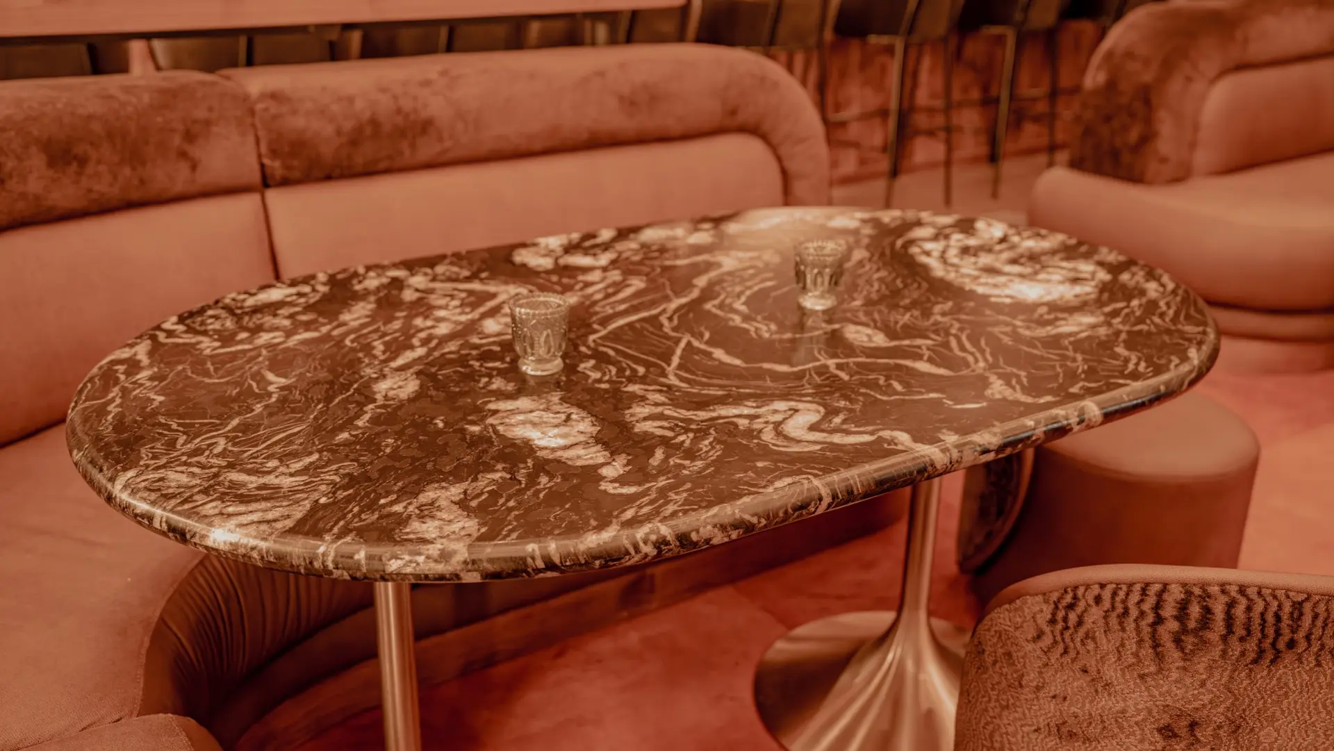 Oval lounge table with a dark stone top swirled with cream veining, set between velvet booths
