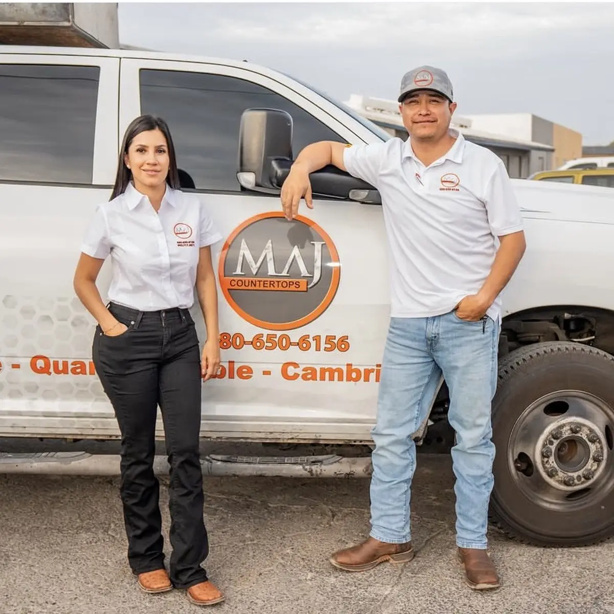 Two MAJ Countertops team members in company shirts leaning on a branded work truck